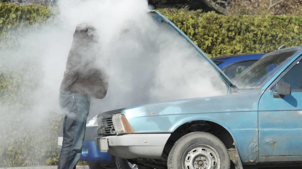 el humo cubre a un hombre mientras abre el capó del coche