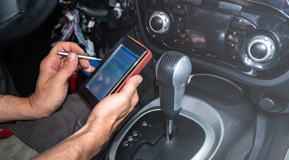 Diagnóstico de averías en el coche: un electricista vestido de gris está sentado en el interior del coche y lee los códigos de avería de un escáner de coche portátil con interfaz OBD2.