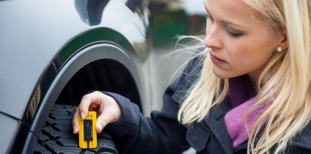 una mujer mide la banda de rodadura de un neumático de coche