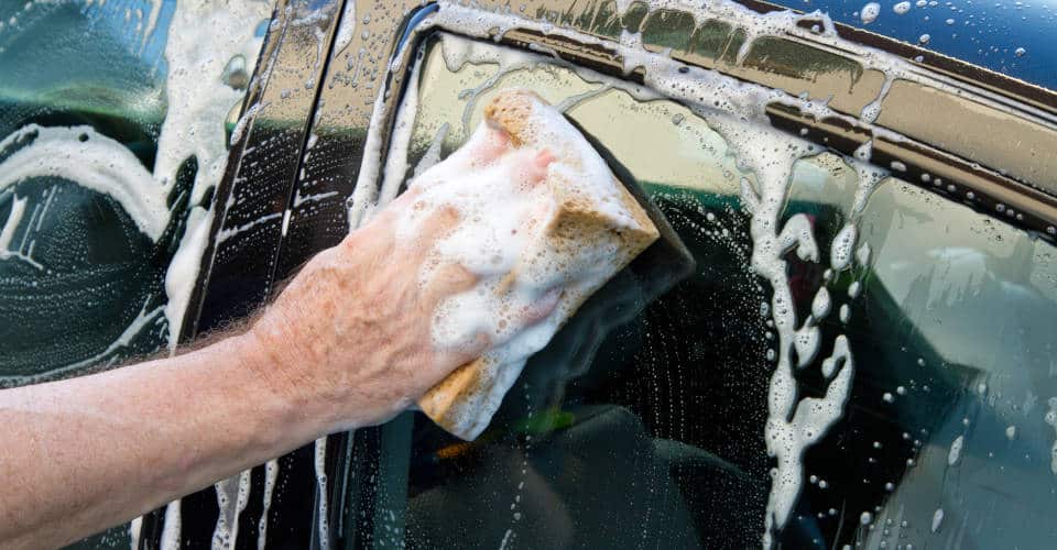 mano con esponja jabonosa lavando el coche
