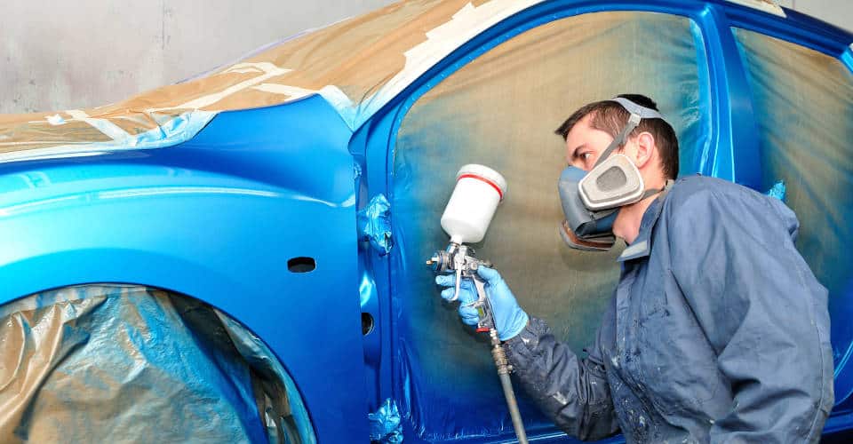 Trabajador pintando un coche azul.